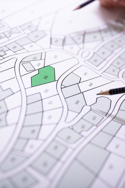 Close-up Of Human Hand Holding Pencil Over Paper Cadastre Map