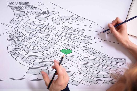 Close-up Of Human Hand Holding Pencil Over Paper Cadastre Map